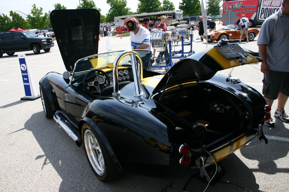 Black-and-yellow Cobra-style roadster, rear 3/4 view at a car show