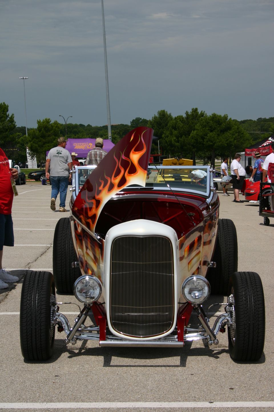 Front of candy-red flamed hot rod roadster with open hood at a car show