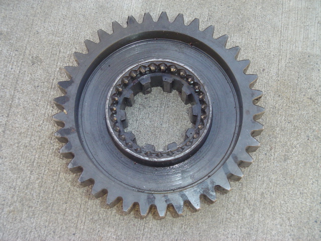 Metal gear with teeth and a splined inner hub, resting on a concrete surface
