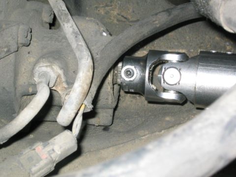 1989 Ford Bronco - Close-up of a new steel steering shaft U-joint with pinch bolt and splined coupler installed near the firewall, routed past a rubber hose a…
