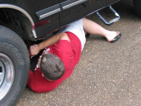 1988 Ford Bronco - A person is seen working on the underside of a black vehicle, with a focus on the tire and chassis components.