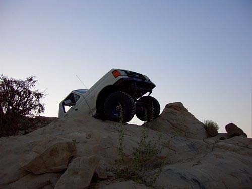 White lifted 4x4 perched on sandstone rock ledge at dusk, rear three-quarter view