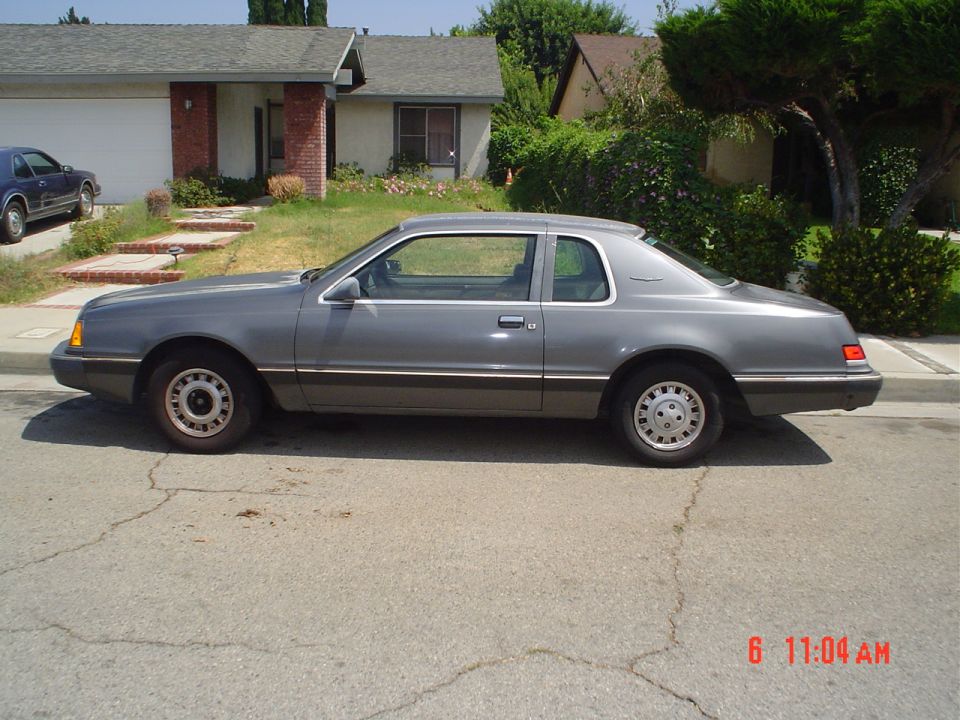 Gray two-tone Ford Thunderbird coupe parked in side profile on a residential street.