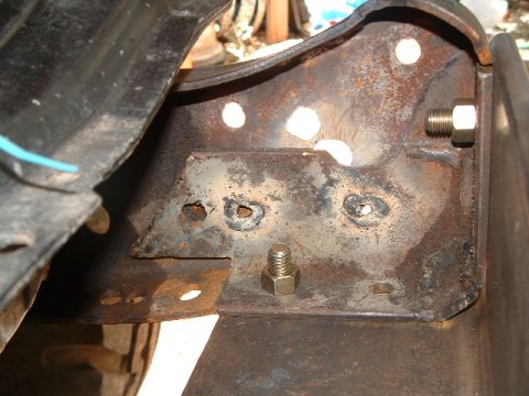 1979 Ford Bronco - Close-up view of a heavily rusted metal bracket with bolts, likely part of a winch system.
