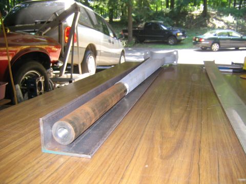 1978 Ford Bronco - A steel angle-iron rail lies on a wood-grain tabletop with a threaded round steel bar and a fabricated bracket resting in the channel, appe…