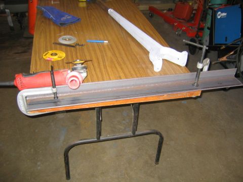 1978 Ford Bronco - A red Craftsman angle grinder with a cutoff wheel rests on a length of steel angle iron clamped to a wood-grain folding table in a workshop…