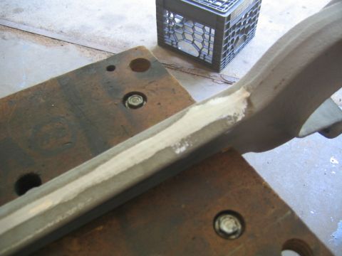 1978 Ford Bronco - A metal suspension arm or bracket clamped in a vise, with fresh tan-colored body filler or primer applied along one edge, undergoing repair…