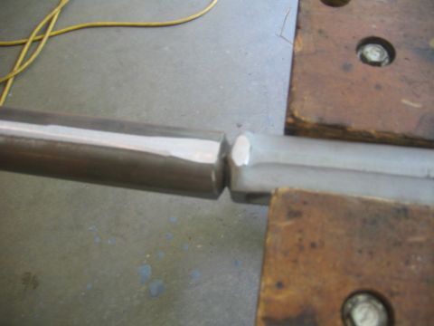 1978 Ford Bronco - Close-up of two metal shafts joined at a hex-shaped coupling or fitting, resting on a workbench with copper welding plates nearby. A yellow…