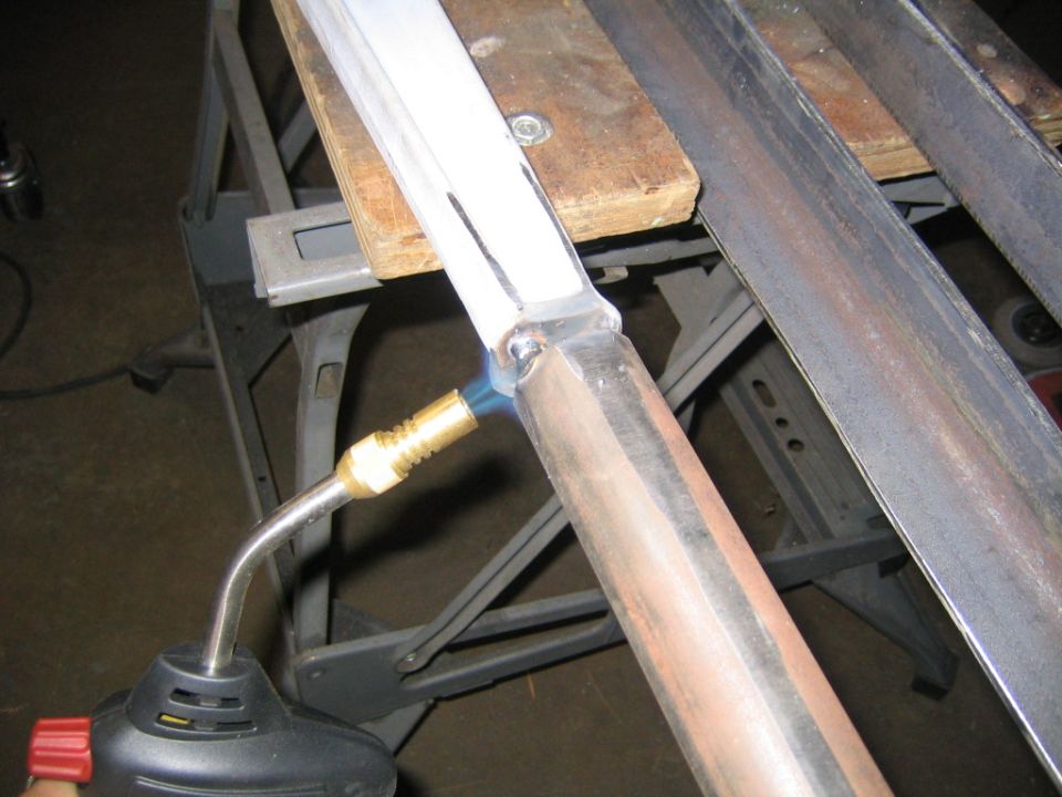 Propane torch heating a metal joint between two bars on a sawhorse in a garage