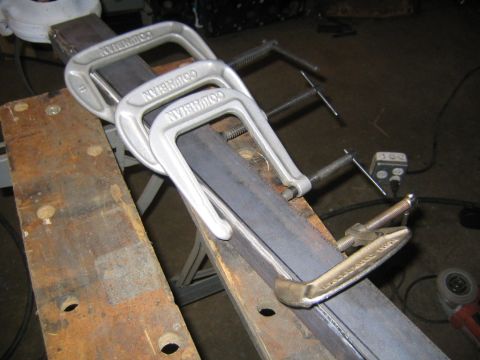 1978 Ford Bronco - Three Columbian C-clamps and a smaller locking-style clamp secure two flat steel bars together atop a worn wooden workbench, likely part of…