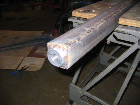 1978 Ford Bronco - A square steel tube axle or arm section with a welded end cap featuring a threaded bung/hole, resting on wood-topped sawhorses or a lift st…