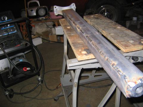 1978 Ford Bronco - A long steel tube or beam with a heavy welded seam bead running its length rests on wooden boards atop a folding sawhorse work stand, likel…