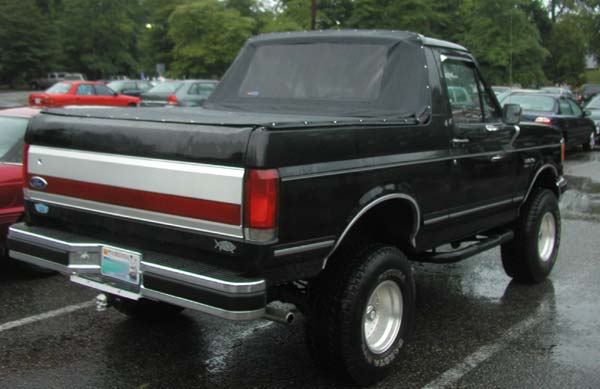 Rear three-quarter view of a lifted black Ford Bronco with soft top and tonneau cover