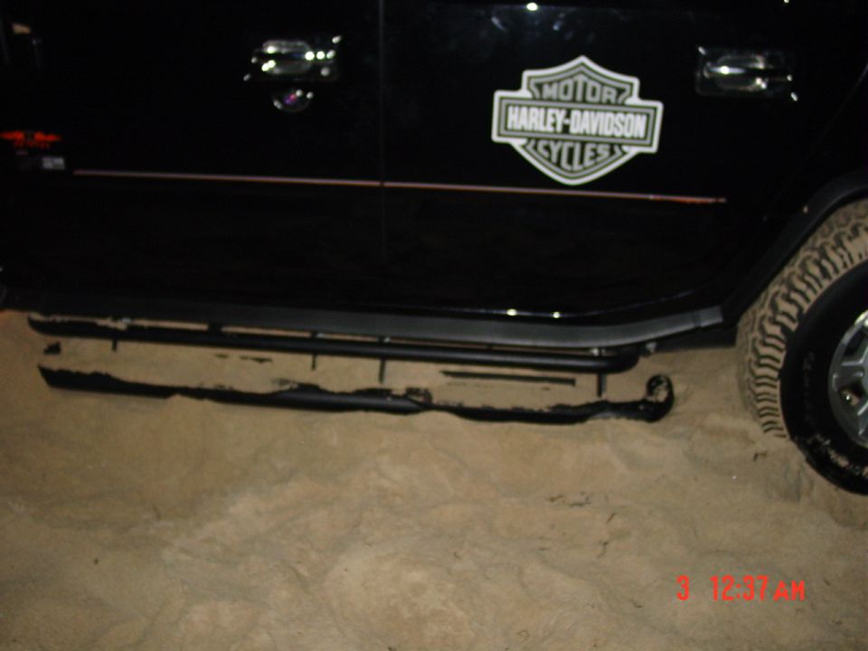 Black SUV side with Harley-Davidson door decal and tubular step bar on sand at night