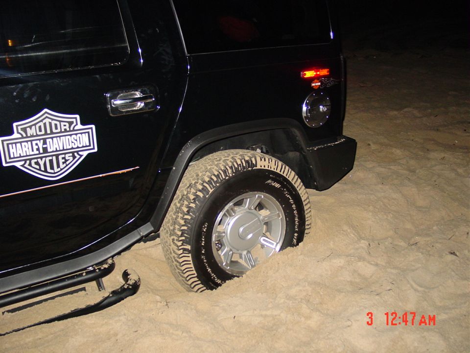 Black Hummer with Harley-Davidson decal stuck in deep sand at night
