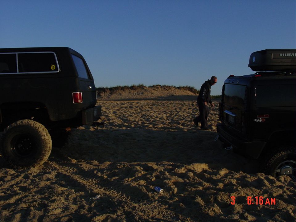 Two dark SUVs parked on sand at dawn with a person walking between them