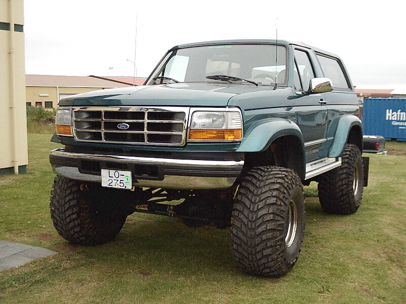 Teal lifted two-door Ford Bronco on large off-road tires, front 3/4 view on grass