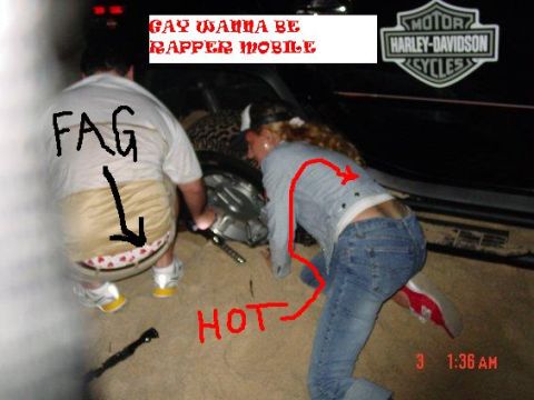 1985 Ford Bronco - A person with text written on their back and underwear visible is being helped by another person to change a tire.