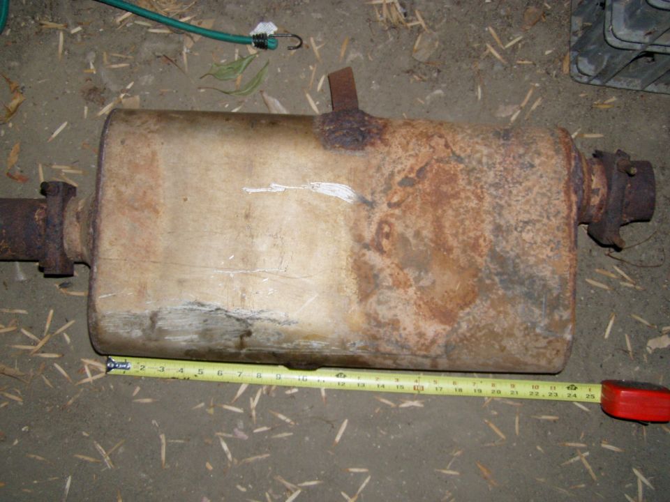 Rusty muffler on dirt with tape measure showing ~25 inch length
