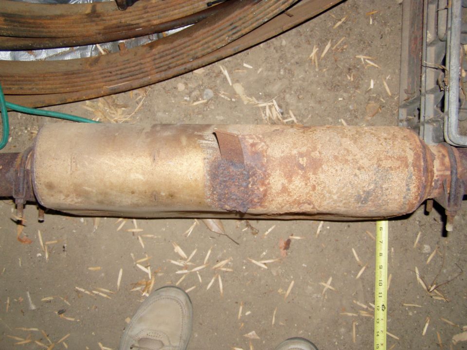 Rusty cylindrical exhaust muffler on pipe with tape measure alongside