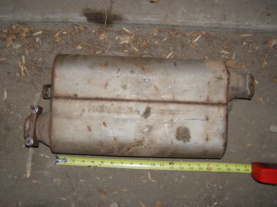 Rusty Flowmaster muffler on concrete with a tape measure showing about 20 inches