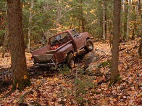 1980 Ford F-100 - A 1980 Ford F-100 tackles a challenging off-road path through a wooded area covered in autumn leaves.