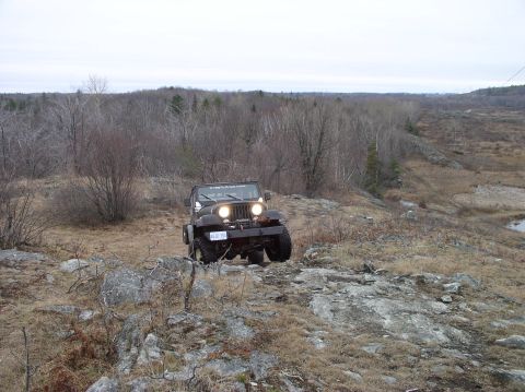 1980 Ford F-100 - A black Jeep Wrangler navigates a rocky, wooded landscape under an overcast sky.