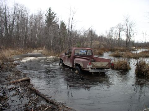 1980 Ford F-100 - Ford F-100 navigates an icy water crossing in a wooded area.