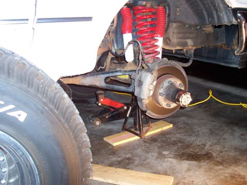 1994 Ford Bronco - Close-up of a vehicle's suspension and brake system, with the wheel removed and supported by a jack stand.