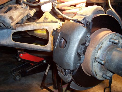 1994 Ford Bronco - Vehicle brake caliper and rotor assembly shown with a jack and jack stand supporting the vehicle.