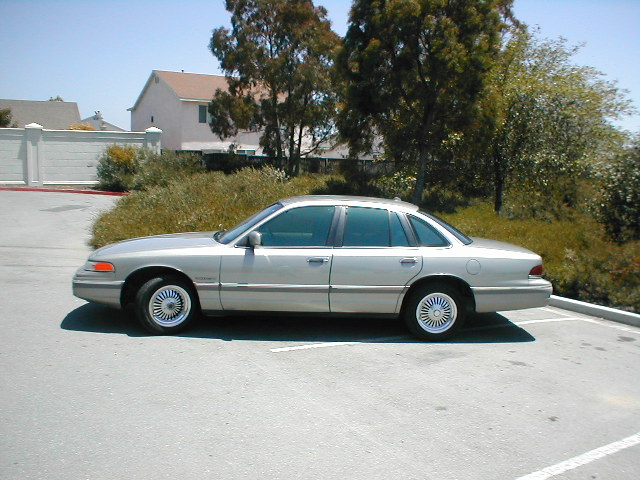 Silver sedan parked on asphalt, side view. Tinted windows, chrome wheels