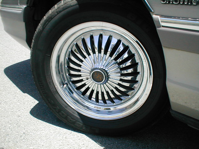 Close-up of a chrome wire wheel with black spokes on a car. Text on the tire is visible