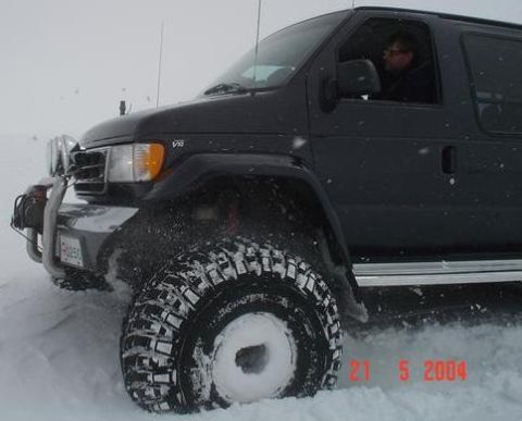 1996 Ford Bronco - A dark van equipped with off-road tires navigates through a snowy landscape.