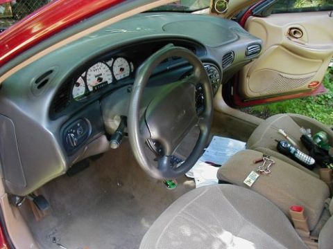 1997 Ford Taurus - The interior of a 1997 Ford Taurus is visible, with the dashboard, steering wheel, and seats in focus. Various items are scattered on the p…