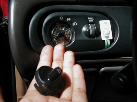 1997 Ford Taurus - A hand holds a removed light switch knob near the dashboard controls, which include a panel dimmer and headlight switch.