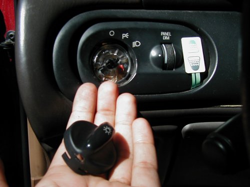 Hand holding light switch knob near dashboard panel dimmer and headlight controls