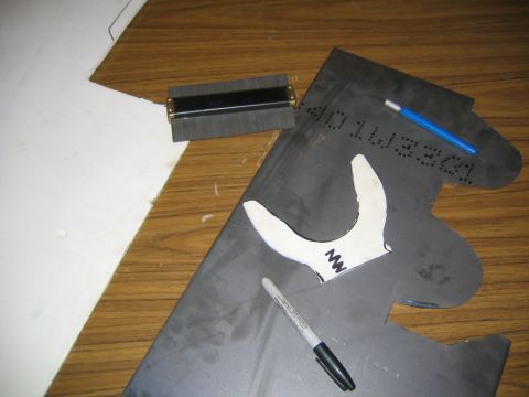 1978 Ford Bronco - A dark gray sheet metal panel with a curved, dual-pronged white cardboard template laid on top, apparently being traced for fabricating a s…