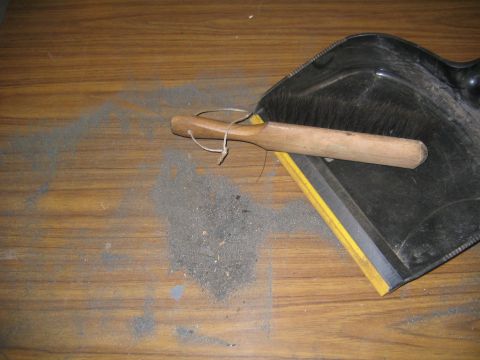 1978 Ford Bronco - A black metal dustpan and a wooden-handled brush rest on a wood-grain surface next to a pile of swept gray dust and debris.