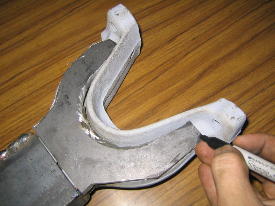 Hand marking a welded U-shaped steel bracket with a Sharpie on a wood table