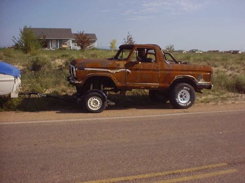 1988 Ford Bronco - This heavily rusted pickup truck, likely from the late 1970s, is being towed down a highway.