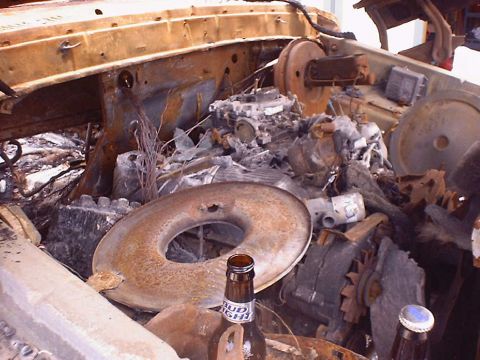 1988 Ford Bronco - The engine bay of a vehicle is heavily damaged by fire, with a Bud Light bottle resting near the air cleaner.