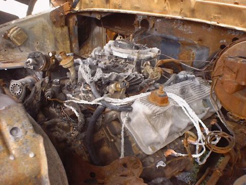 1988 Ford Bronco - The engine compartment of a vehicle shows extensive fire damage, with charred components and melted wiring visible.