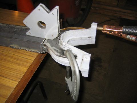 1978 Ford Bronco - A steel weldment being fabricated on a workbench, held together with a white magnetic welding square and an aluminum C-clamp while a copper…