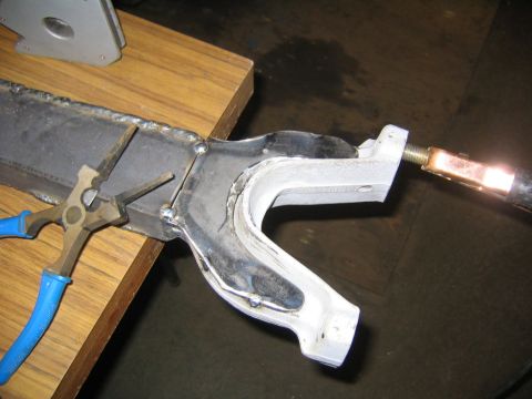 1978 Ford Bronco - A fabricated metal suspension arm or bracket clamped in locking pliers on a wooden workbench, being heated with a gas torch flame at the th…