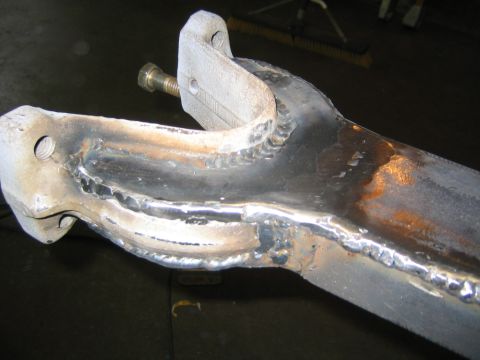 1978 Ford Bronco - Close-up of a fabricated steel suspension arm or bracket assembly with fresh MIG weld beads joining a forked mount and a tab with mounting…