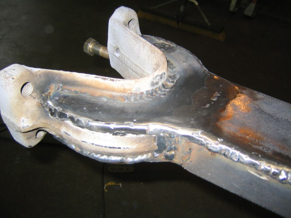 Welded steel suspension arm bracket with fresh weld beads and a mounting bolt