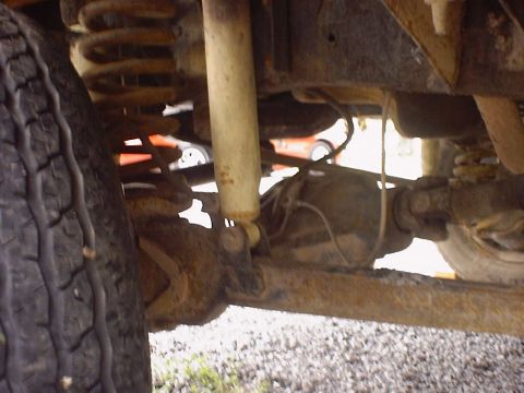 1988 Ford Bronco - The underside of a vehicle shows its suspension components and a portion of the rear axle, with another vehicle in the distance.