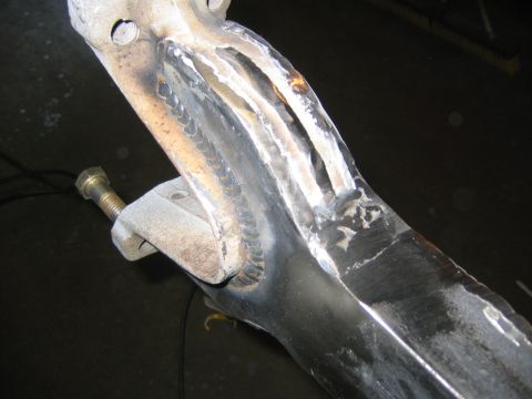 1978 Ford Bronco - Close-up of a welded steel suspension arm or axle component with visible MIG weld beads joining reinforcement plates. A bolt with a brass-c…