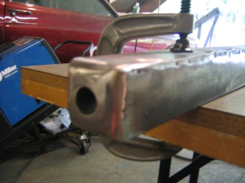 1978 Ford Bronco - A fabricated steel box tubing section with welded seams and a large drilled hole in the end, clamped with a C-clamp to a wooden workbench.…