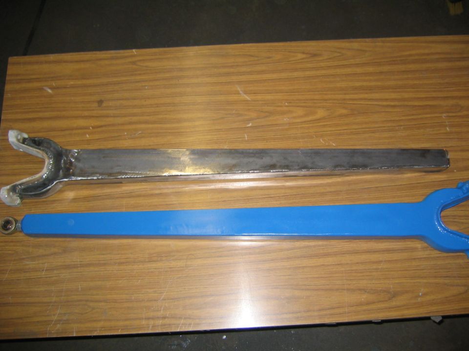 Bare steel and blue-painted forked suspension radius arms on wood table